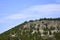 Limestone mountainside covered with pine trees. Natural landscape against the blue sky with blurry clouds