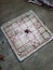 Line drawing of a chowka bara or ludo board. Used tamarind seeds as a dice for a game. Players using different types of objects as