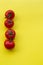 Line of four tomatoes on yellow background, copy space