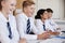 Line Of High School Students Wearing Uniform Sitting At Desk In Classroom