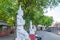 Line of white Buddha image statues lining one side of a short road.