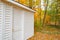 Lines of boards of white wooden building standing among trees in autumn colors and surrounded by leaf drop