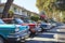 A lineup of classic cars from different eras parked neatly along the side of a bustling urban street, A mid-century American