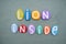 Lion inside, motivational slogan composed with multi colored stone letters over green sand