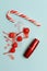 Lipstick in red tube, cocktail cherries with spilled syrup and candy cane on light blue background