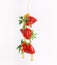 Liquid honey flows and dripping on flying strawberries at white background. Delicious healthy summer fruit. Food levitation.