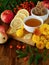 Liquid honey in a little bowl surrounded by slices of lemon, apples, rowan berries and flowers