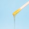 Liquid yellow wax or sugar paste for depilation drains from the stick on blue background. The concept of depilation, waxing,
