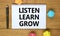 Listen, learn, grow symbol. Words `Listen, learn, grow` on white note on beautiful wooden table, colored paper, black metallic p