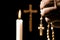 Lit candle and hand holding a rosary on a crucifix background, i