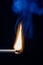 Lit matchstick  with blue smoke on a black background