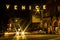 Lit street sign over cars` starburst lights mark entrance to Venice Beach, California