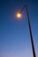 Lit tall street light post or pole illuminating a road at dusk. Wide, low-angle view, no people