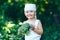 Litle happy smiling farmer boy in white overalls and grey hairband holding fresh organic broccoli in hands. garden, harvest season