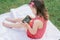 Little 3-4 girl in red clothes sits on blanket on green grass and looks into mobile phone. Children, using gadgets