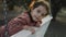 Little 5 yo girl having fun on a white swing in a quiet, tree-lined park background. Preschooler relaxing on a bench