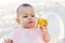 Little 8 month old girl eats. With astonishment and admiration, baby considers a banana on the beach