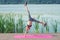 A little acrobat girl is standing on her hands and doing the acrobat trick in the air on a pier near the lake