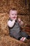 Little adorable baby boy sits near haystacks indoor and looks serious eyes