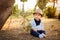 Little adorable baby boy in a straw hat and blue pants sitting w