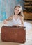 Little adorable ballerina in white tutu with old vintage suitcase in a beautiful studio. Travel and voyage