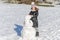 Little adorable girl child sculpts snowman from snow in winter