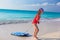 Little adorable girl pulls a surfboard on white shore