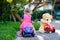 Little adorable toddler girl driving toy car and having fun with playing with plush toy bear, outdoors. Gorgeous happy