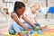 Little african american girl and classmate playing with colourful educational toy blocks on the floor at preschool or