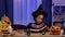 Little African American girl in festive costume reads book with enthusiasm. Child sits at table in room decorated for