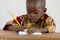 Little African Black Baby Boy in the Classroom Writing Notes