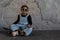 Little African kid boy with dreadlock hairstyle wear cool gold sunglasses, necklace chain, jeans bib and sneaker smiling