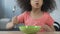 Little Afro-American girl sitting at the table with spoon and asking for dinner