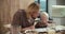 A little albino boy with white hair reads a book with his father, a blond man with glasses and a beard, in the kitchen