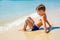 Little alone boy sitting on beach near water