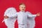 Little angel kid isolated. Valentines day. Cute child boy in white dress standing over red.