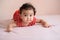 Little Asian baby, cute toddler dressed in red practicing crawling on the bed and looking at the camera