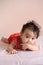 Little Asian baby, a cute toddler dressed in red practicing crawling and bite her hand on the bed and looking at the camera