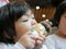 Little Asian baby girl, 2 years old, feeling blissful eating / biting ice cream cone - facial expression of joyfulness