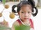Little Asian baby girl, 42 months old, looking at a longan fruit, as she is trying to pick it from its branch by herself