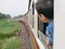 Little Asian baby girl enjoys sticking her head out of a train window and having the wind whips against her face