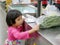 Little Asian baby girl putting Chinese morning glory in plastic bag on a counter for weighing and calculating the price