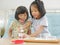 Little Asian baby girl  right  smiling and enjoys scooping her little sister`s ice cream - siblings rivalry / taking advantage