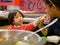 Little Asian baby girl sharing food, hotpot, with her mother