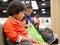 Little Asian baby girl, together with her younger sister, watching a smartphone, same as her mom, sitting and waiting for a queue