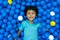 A little Asian boy is playing with a lot of blue and yellow balls