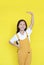 Little asian child girl measures the growth on yellow background. Kid estimate her height by hand with looking camera