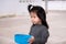 Little Asian child holding blue bowl. Black haired girl was helping with housework by using water dipper in front of the house.