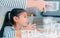 Little Asian girl curiously watching her mother making bread and flour in home kitchen