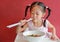 Little asian girl eating Egg noodle with roasted duck and pork on high chair against red wall background